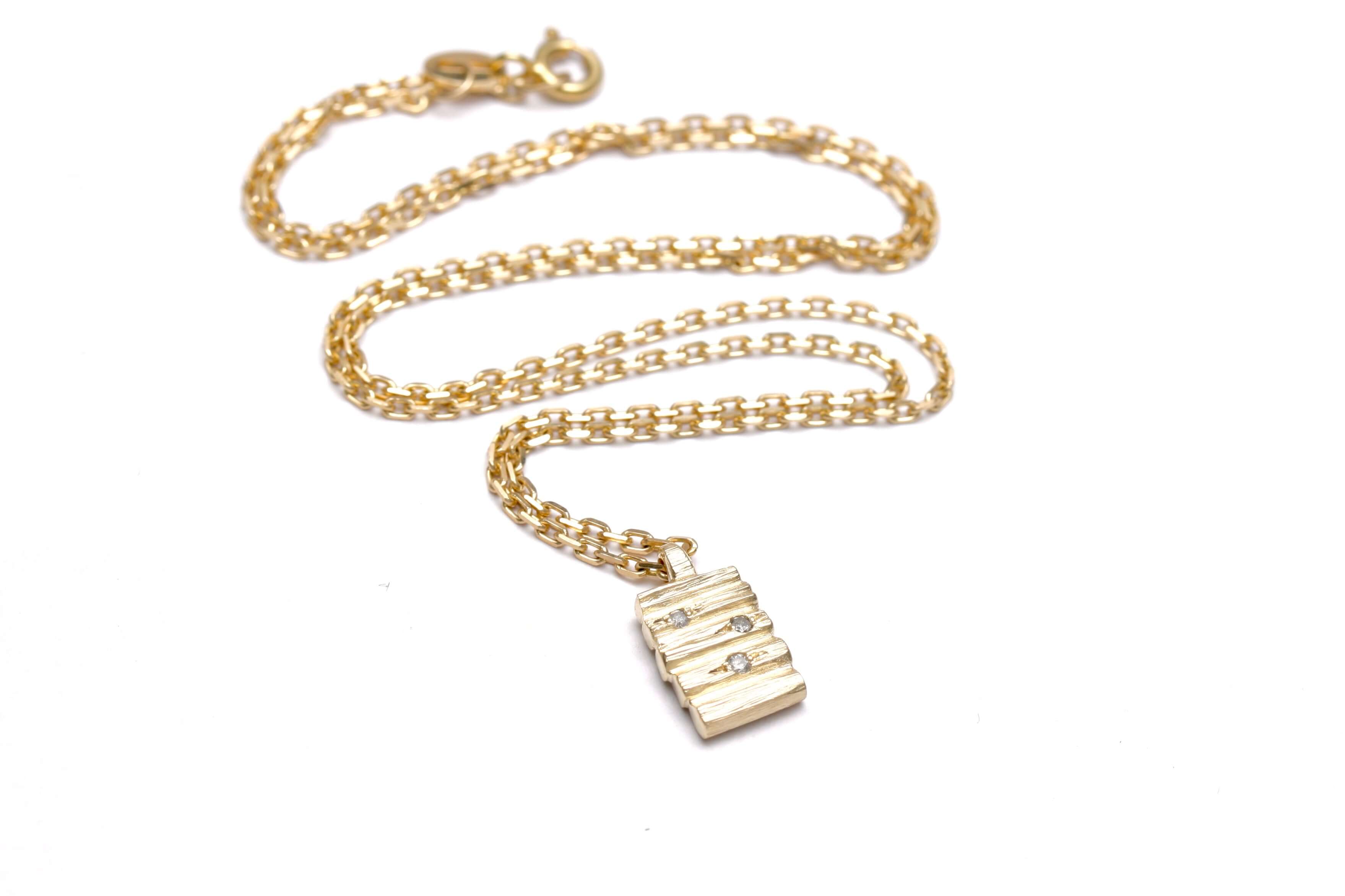 Henge pendant featuring stacked lithic columns and salt and pepper diamonds on a 9 carat yellow gold chain.